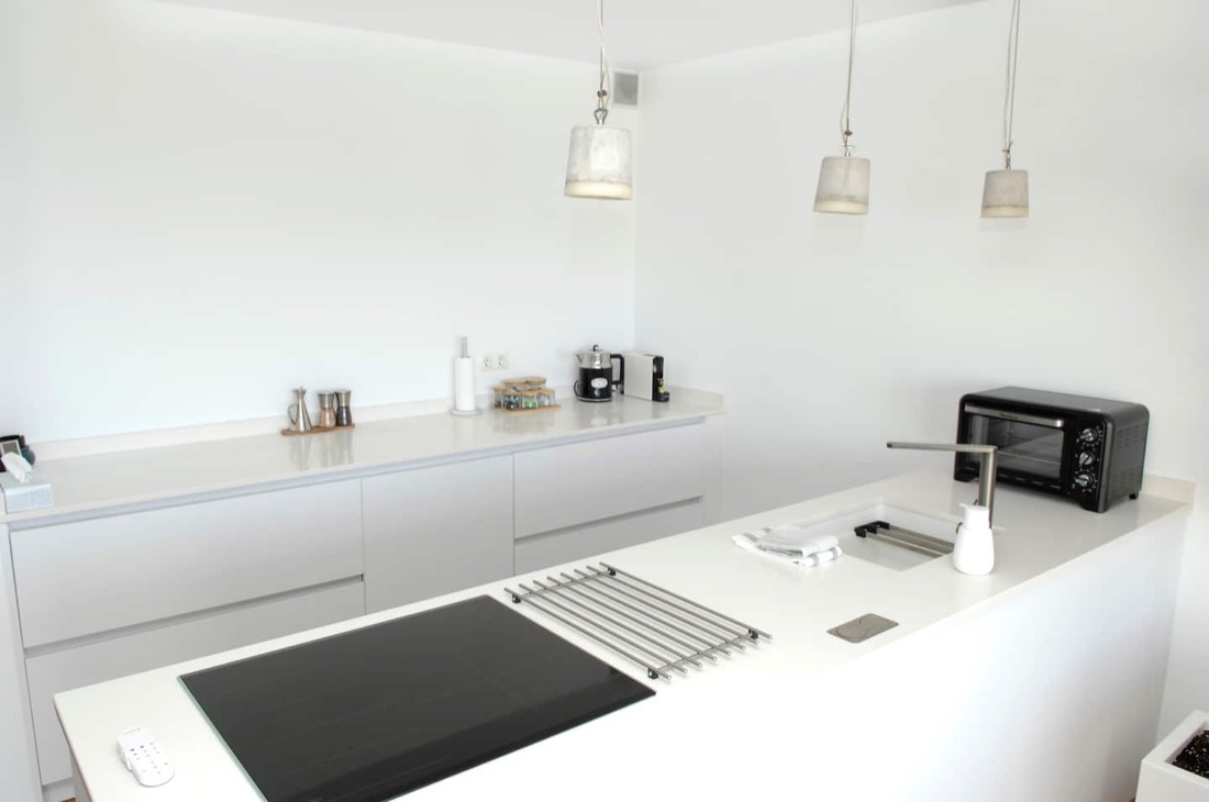 Moderne keuken met koelkast, oven, afwasmachine, Nespresso machine, waterkoker, inductie kookplaat, broodrooster, blender, rijstkoker, sinaasappelpers, pannen, borden, glazen, bestek.